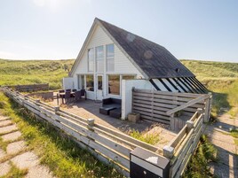 A house with a sloped roof, large windows, and a patio area with outdoor furniture.
