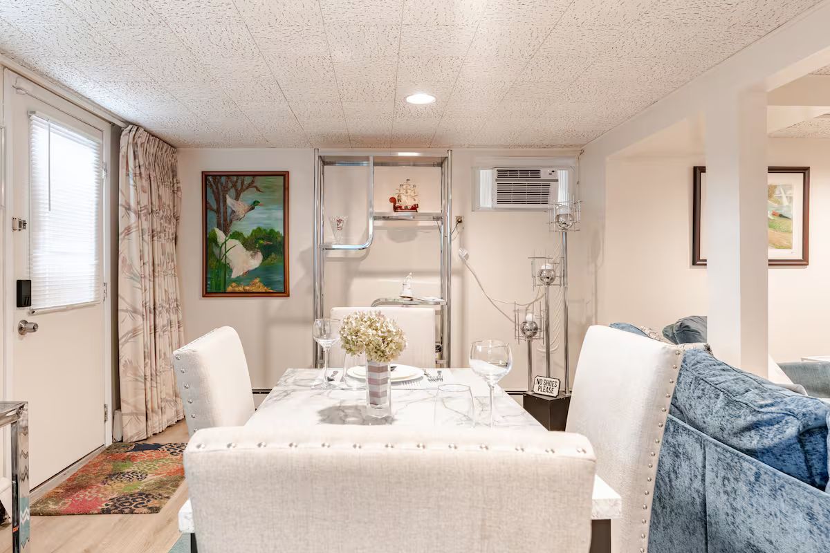 A dining area with a table set for two, a sofa, and a painting on the wall.