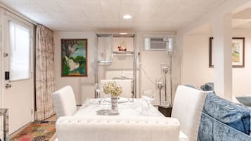 A dining area with a table set for two, a sofa, and a painting on the wall.