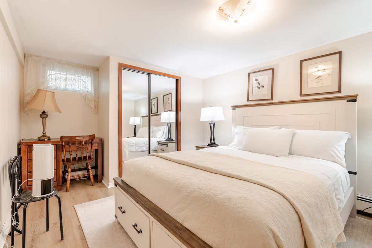 Een slaapkamer met een groot bed, nachtkastjes, een spiegel, een bureau met stoel en een raam met gordijnen.