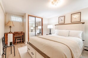 A bedroom with a large bed, bedside tables, a mirror, a desk with a chair, and a window with curtains.