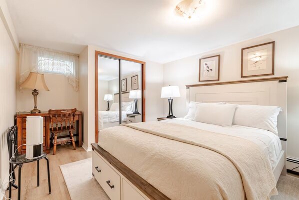 A bedroom with a large bed, bedside tables, a mirror, a desk with a chair, and a window with curtains.