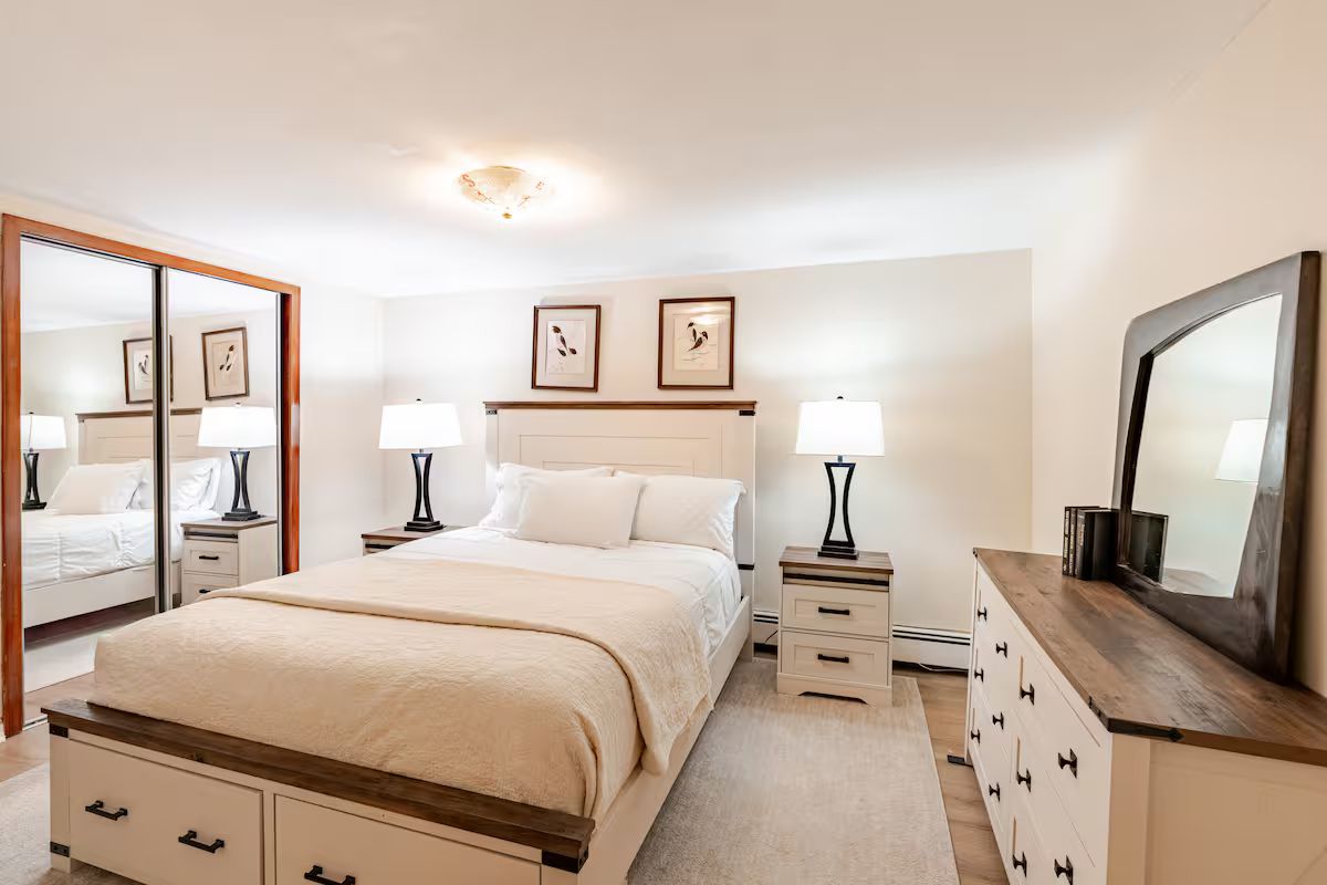 Une chambre à coucher comprenant un lit, des tables de chevet, une commode, un miroir et des tableaux encadrés accrochés au mur.
