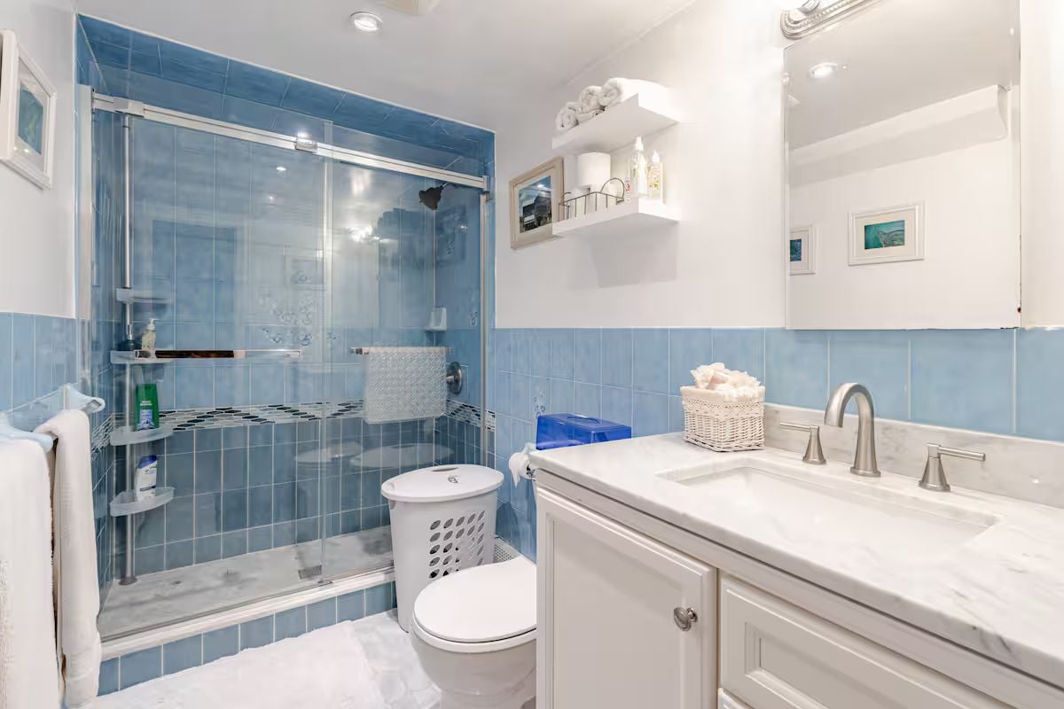 A bathroom with a glass-enclosed shower, a white toilet, a sink with a mirror, and a towel rack.
