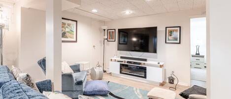 A modern living room with a large flat-screen TV, a sofa, a coffee table, and a patterned rug.