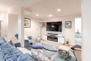 A modern living room with a large flat-screen TV, a sofa, a coffee table, and a patterned rug.
