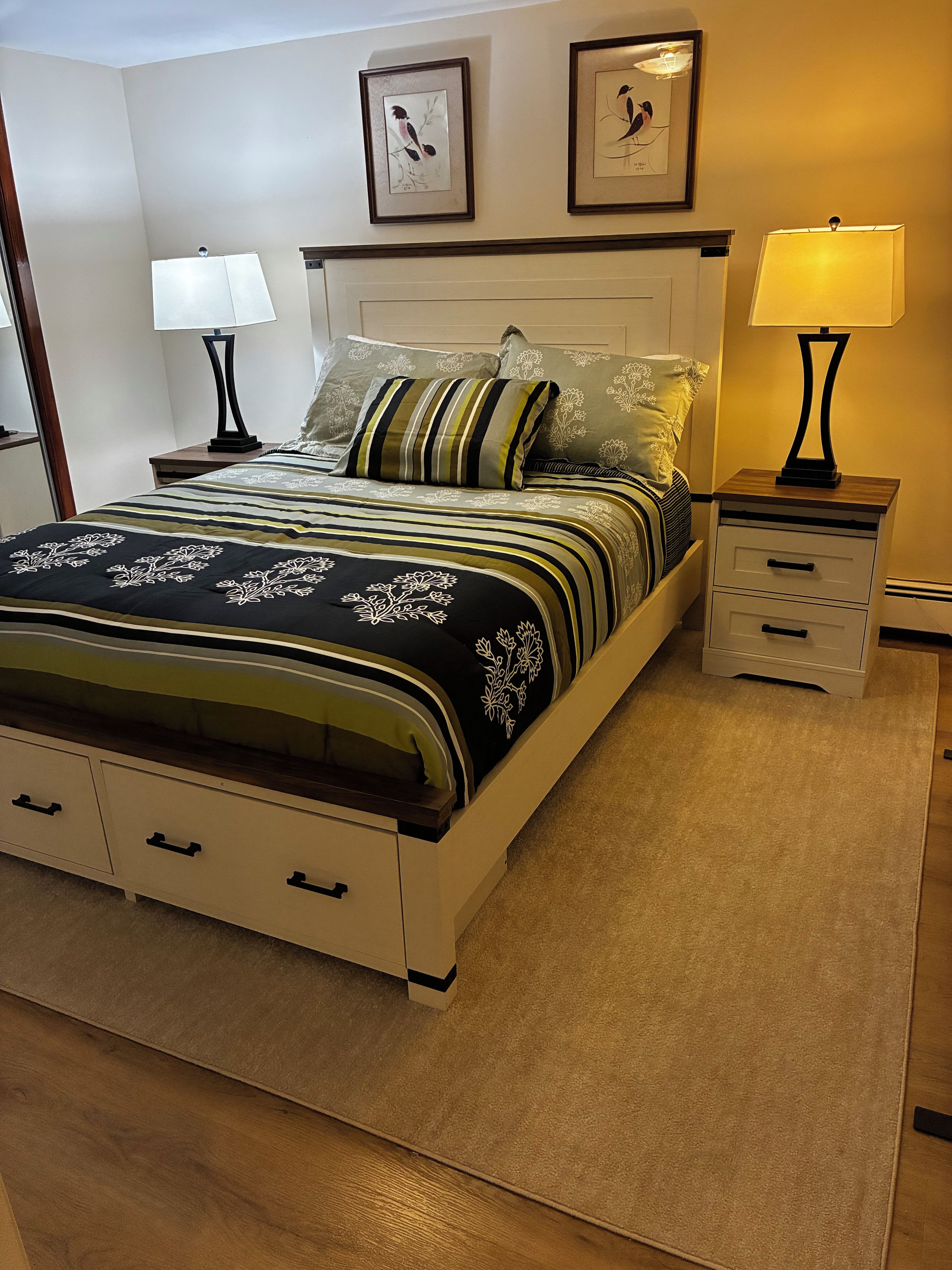 A neatly made bed with a striped bedspread, two bedside tables with lamps, and two framed pictures on the wall.