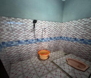 Un baño pequeño con paredes de baldosas a cuadros, una ducha, un cubo y un inodoro.