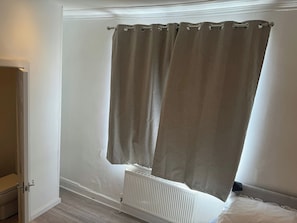 A room with a white radiator, a door, and a window with beige curtains.