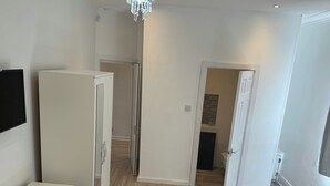 A room with a wooden floor, white walls, a white wardrobe, and a door leading to a bathroom. - 4-bed House - Ensuite Rooms - Sleeps 8 - Parking (Manchester)