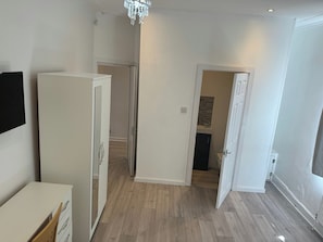 A room with a white wardrobe, a door leading to a bathroom, and a wooden floor.