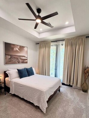 Ein Schlafzimmer mit Bett, Deckenventilator, einem Gemälde und Vorhängen.