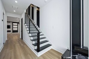 Eine moderne Treppe mit schwarzen Geländern und Holzstufen, die zu einem Raum mit Flachbildfernseher und Regalen führt.