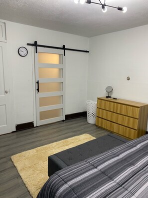 Een slaapkamer met een bed, een dressoir, een spiegel, een klok en een schuifdeur.