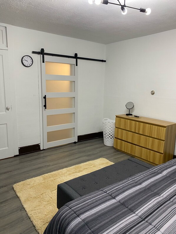 Une chambre à coucher comprenant un lit, une commode, un miroir, une horloge et une porte coulissante.