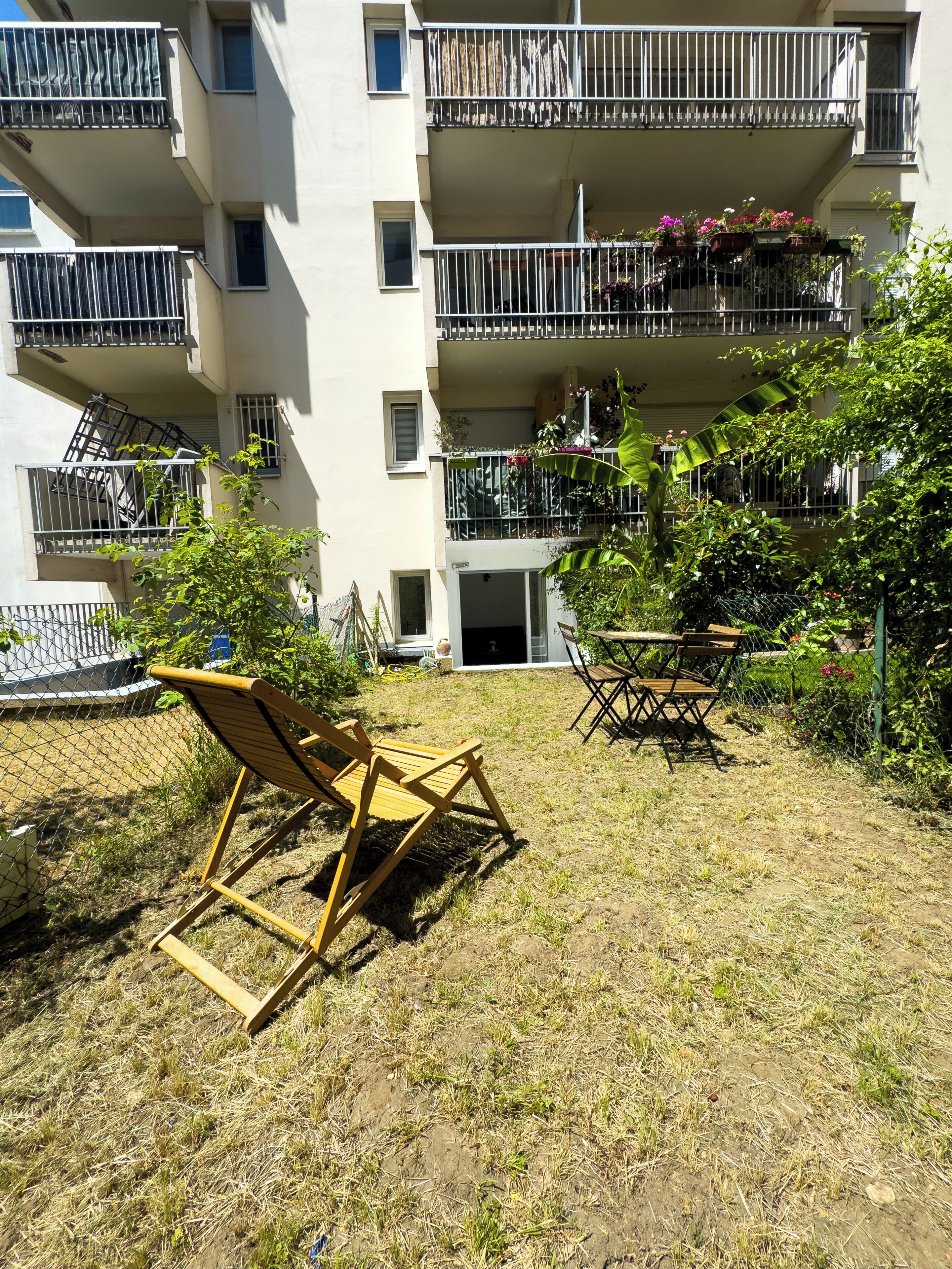 A multi-story residential building with balconies, outdoor seating, and a fenced yard.
