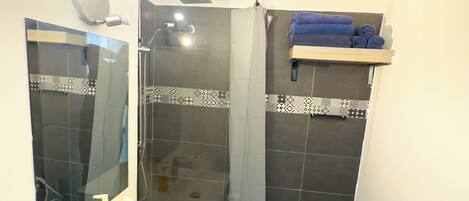A bathroom with a white sink, a mirror, a shower with a glass door, and a towel rack with towels.