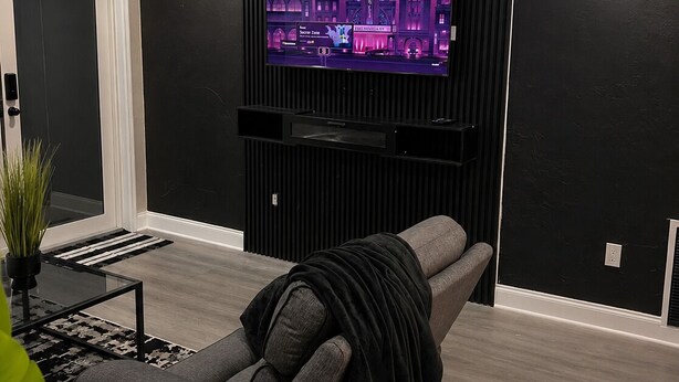 A modern living room with a reclining chair, a flat-screen TV mounted on a black wall, and a small table with a plant. - Signature Stay 5 Minutes From Hard Rock Stadium (Miami Gardens)