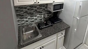 Une cuisine compacte avec des meubles blancs, un four à micro-ondes, une cuisinière, un évier et un réfrigérateur.