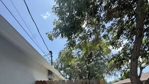 Une cour arrière clôturée avec un chemin de gravier, un arbre et un bâtiment blanc en arrière-plan.