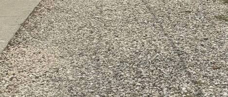 A residential driveway with gravel, a garage door, a wooden fence, and a tree.