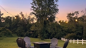 An outdoor seating area with four Adirondack chairs and a square table, surrounded by a wooden deck and a white picket fence. - River Edge Retreat - Private Waterfront & Fire Pit (Jacksonville)