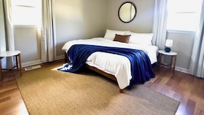 A bedroom with a bed, a ceiling fan, a round mirror, and two bedside tables. - River Edge Retreat - Private Waterfront & Fire Pit (Jacksonville)