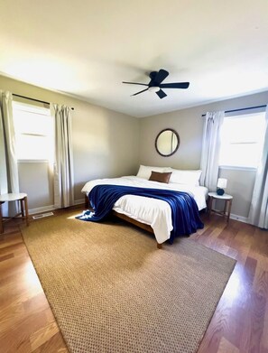 A bedroom with a bed, a ceiling fan, a round mirror, and two bedside tables. - River Edge Retreat - Private Waterfront & Fire Pit (Jacksonville)