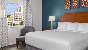 A hotel room with a large bed, two bedside lamps, a chair, and a view of buildings outside.