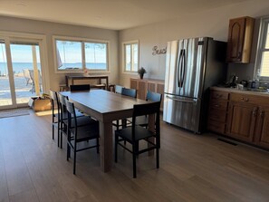 Eine moderne Küche mit einer großen Kochinsel, einem Edelstahlkühlschrank, Holzschränken und großen Fenstern mit Blick auf einen Strand.