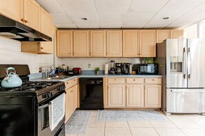 A kitchen with wooden cabinets, a stainless steel refrigerator, a black stove, and a dishwasher.
