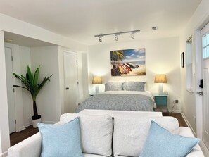 Ein Schlafzimmer mit einem Bett, zwei Nachttischlampen, einem großen Gemälde, einer Topfpflanze und Blick auf den Flur.