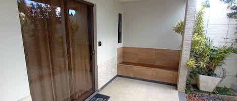 A covered outdoor area with a sliding glass door, a bench, and a small garden with plants.