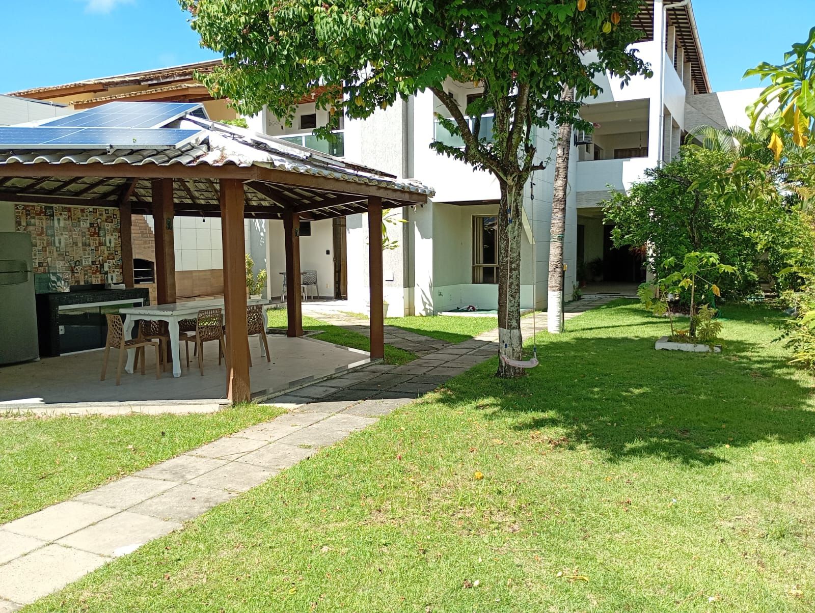 A covered outdoor dining area with a table and chairs, a solar panel, and a small tree.