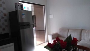 Una sala de estar con un sofá blanco, una mesa con un jarrón de rosas rojas y un refrigerador.