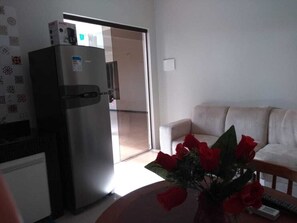 A living room with a white sofa, a table with a vase of red roses, and a refrigerator. - Small and cozy one-bedroom apartment in Stella Maris. Condominium and close to the beach (Salvador)