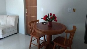 Un comedor con una mesa redonda de madera, cuatro sillas de madera y un jarrón con flores rojas.