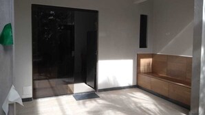 Una habitación con puerta de vidrio corrediza, un banco de madera, suelo de baldosas y un estante pequeño fijado a la pared.