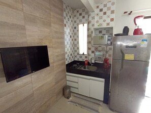 A kitchen with a flat-screen TV mounted on the wall, a refrigerator, a sink, and a microwave. - Small and cozy one-bedroom apartment in Stella Maris. Condominium and close to the beach (Salvador)