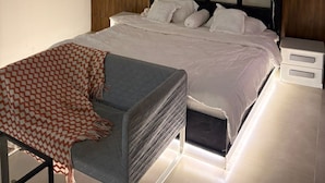 A modern bedroom with a bed, bedside tables, a chair, and a wall-mounted artwork. - OrbitNet-Al Khatim (Madina)