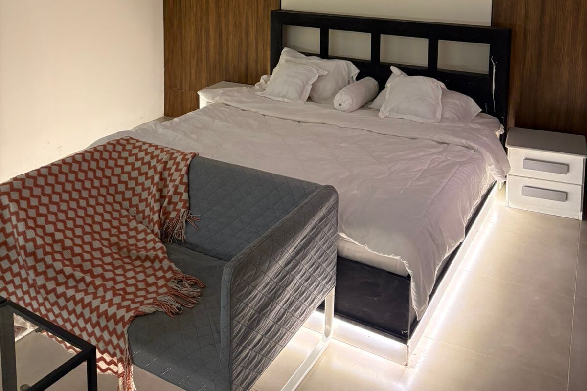 Ein modernes Schlafzimmer mit einem Bett, Nachttischen, einem Sessel und einem Wandbild.