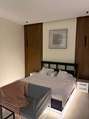 Ein modernes Schlafzimmer mit einem Bett, Nachttischen, einem Sessel und einem Wandbild.