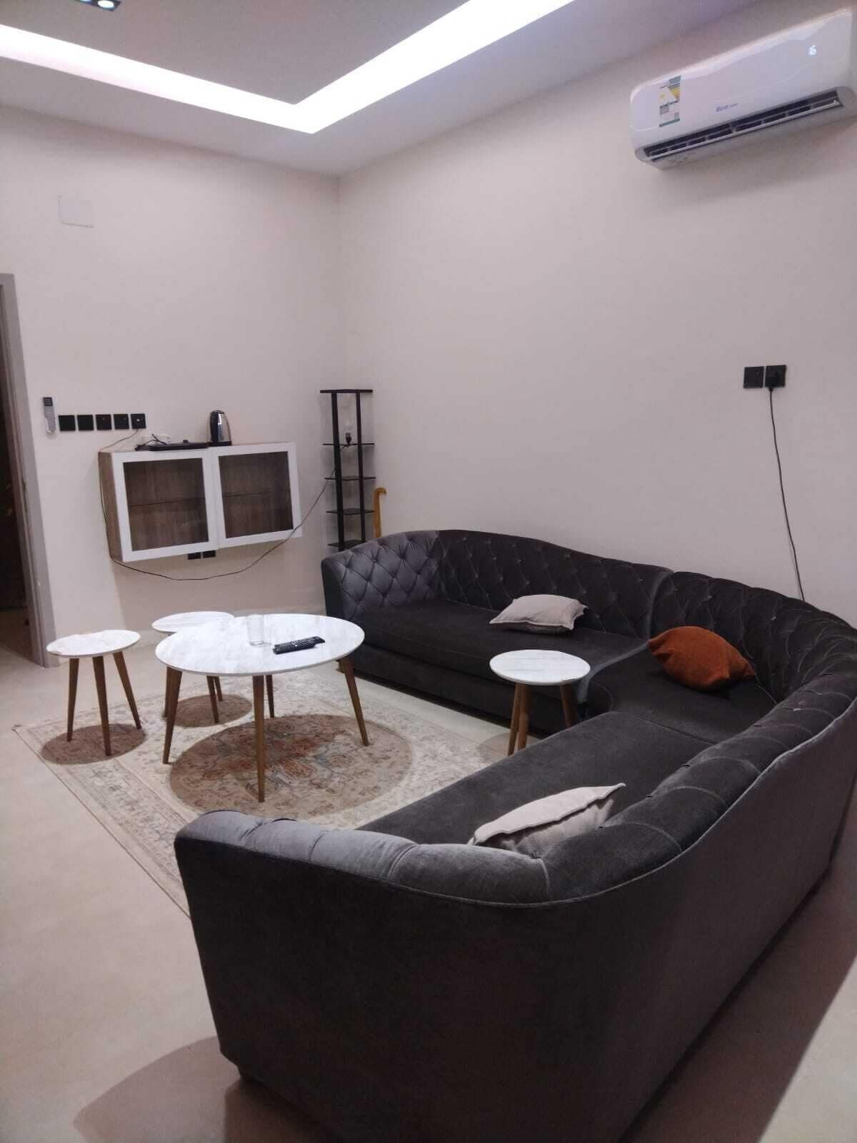 Ein modernes Wohnzimmer mit einem dunkelgrauen Sofa, zwei runden Couchtischen, einem flachbildfernseher an der Wand und einer Klimaanlage.
