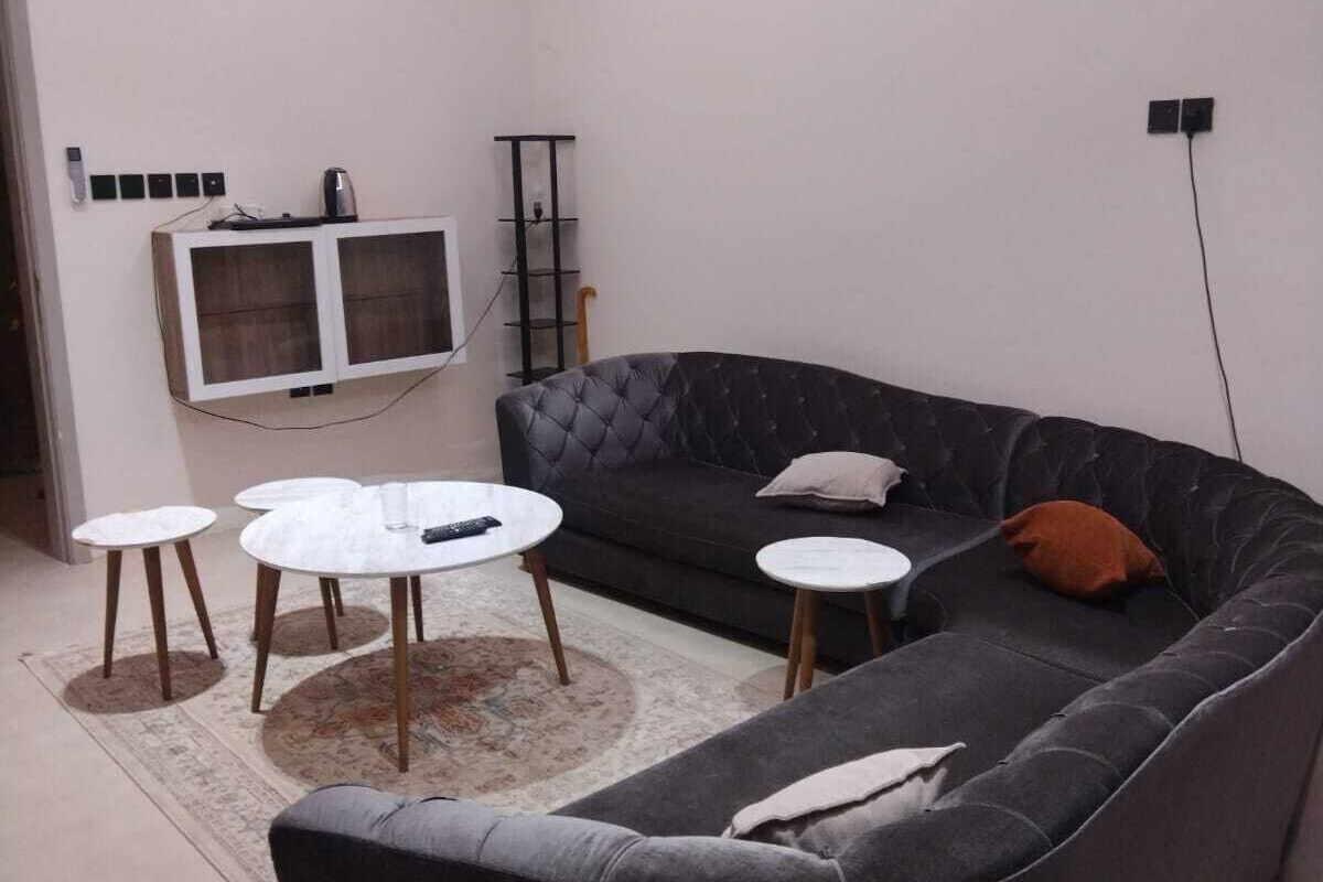 Ein modernes Wohnzimmer mit einem dunkelgrauen Sofa, zwei runden Couchtischen, einem flachbildfernseher an der Wand und einer Klimaanlage.