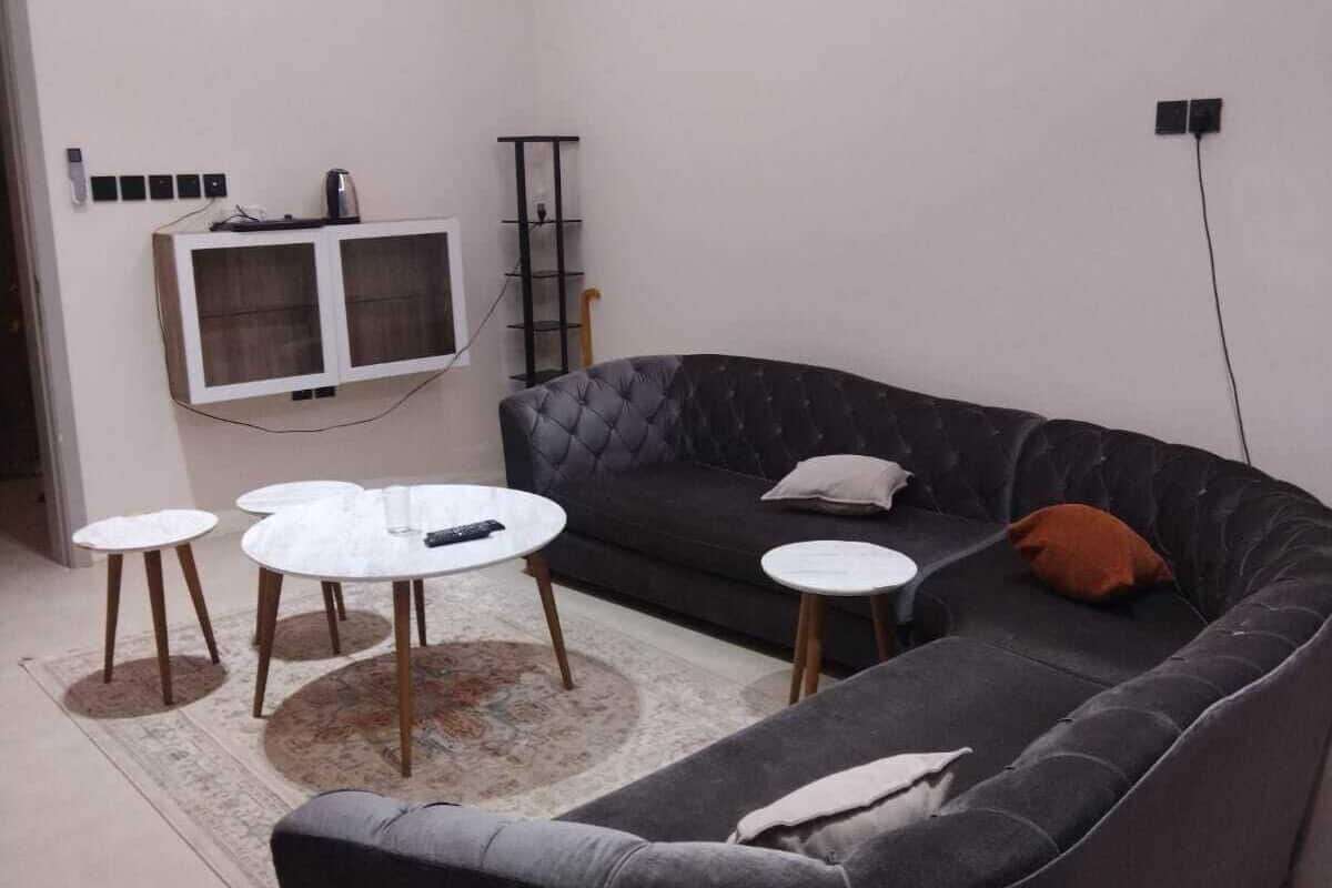 Un saló modern amb un sofà gris fosc, dues taules de centre rodones, un televisor de pantalla plana fixat a la paret i un aparell d'aire condicionat.