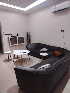Ein modernes Wohnzimmer mit einem dunkelgrauen Sofa, zwei runden Couchtischen, einem flachbildfernseher an der Wand und einer Klimaanlage.