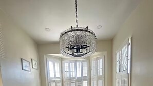 Ein Esszimmer mit Holztisch, sechs Stühlen, einer Chandelierleuchtre und großen Fenstern mit Fensterläden.