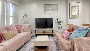 Ein Wohnzimmer mit einer Couch, einem Hocker, einem Fernseher und einem gerahmten Bild an der Wand.