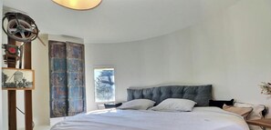A bedroom with a large bed, a window with a view of trees, and a rustic wall with a metal door.