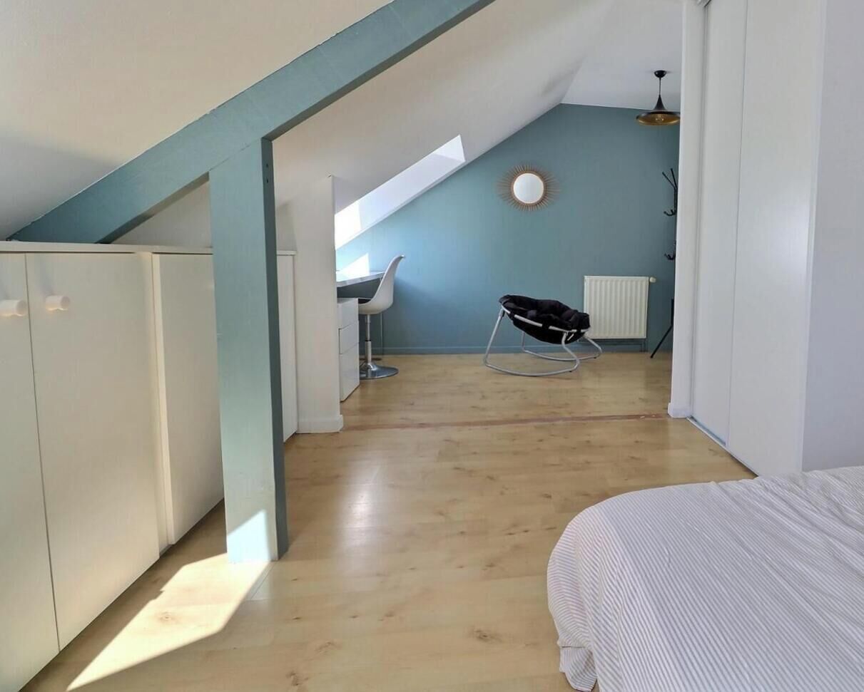 Une pièce avec un plafond en pente, un lit, une chaise et un radiateur.